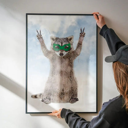 Watercolor raccoon superhero poster with a green mask, making peace signs against a cloudy sky in a black frame.