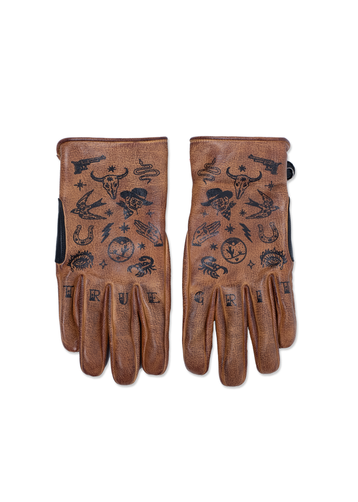 Brown leather gloves with black tattoo-style designs, including skulls, snakes, and stars. "TRUE GRIT" is printed on the fingers.