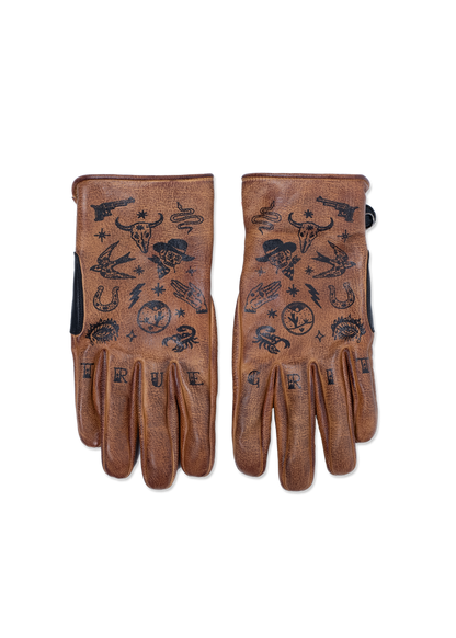 Brown leather gloves with black tattoo-style designs, including skulls, snakes, and stars. "TRUE GRIT" is printed on the fingers.