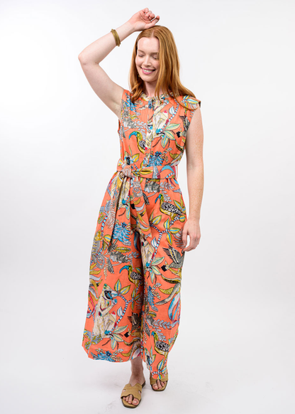 Woman wearing a coral tropical floral print sleeveless jumpsuit with sandals