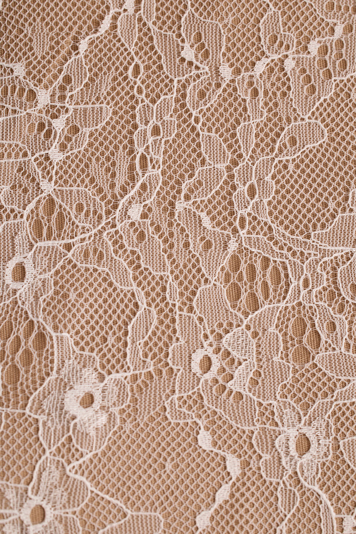 Close-up of white floral lace fabric with netted detail over a tan backing.