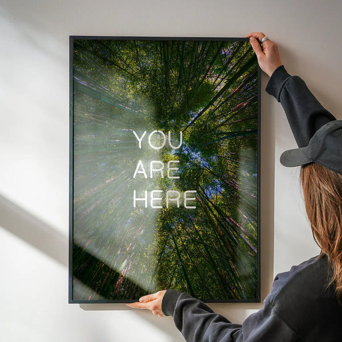 Framed You Are Here neon-style forest print on glossy archival paper held against a white wall.