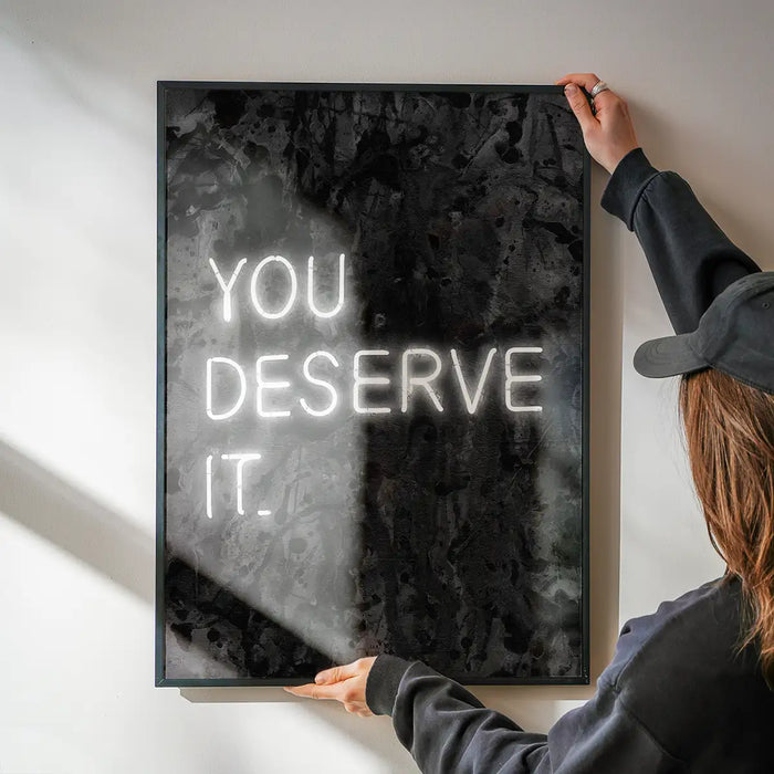 You Deserve It Neon Style Print being hung on a wall in a black frame